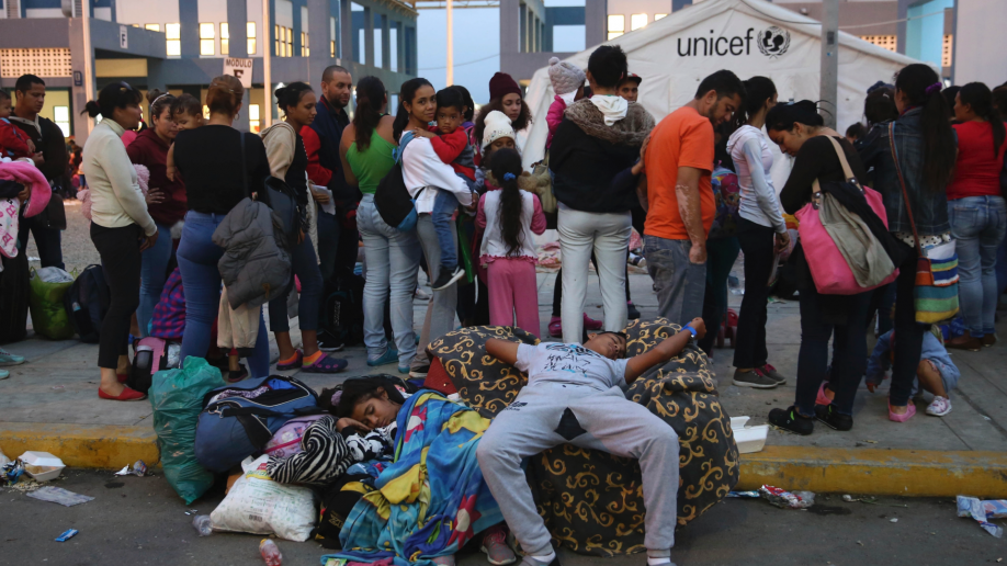 Venezuelan migrants rest while another group stands in line to enter am immigration office in Tumbes, Peru,