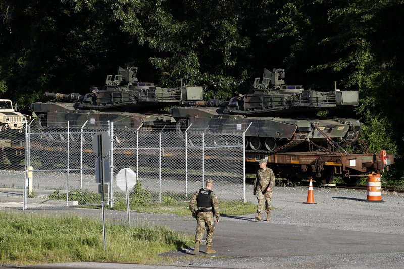 Military police walk near Abrams tanks on a flat car in a rail yard, Monday, July 1, 2019,