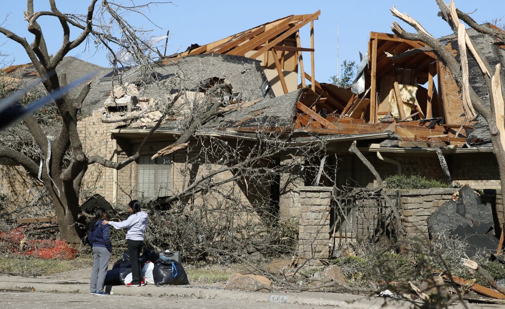 Women stand outside a house damaged by a tornado in the Preston Hollow section of Dallas, Monday, Oct. 21, 2019