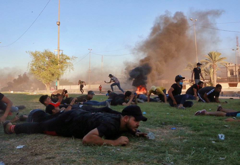 Anti-government protesters take cover while Iraq security forces fire during a demonstration in Baghdad, Iraq, Friday, Oct. 4, 2019.