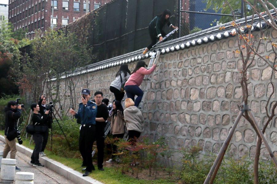 South Korean university students climb over a wall during a protest against the Special Measures Agreement, at Habib House, the U.S. ambassador’s residence, in Seoul on Friday.