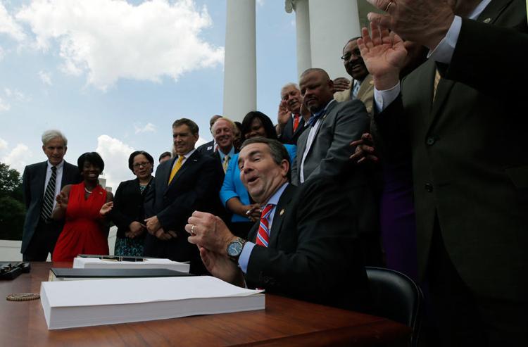 Virginia Governor Ralph Northam, center, reacts after signing the state budget bills that include Medicaid expansion during a ceremony Thursday, June 7, 2018, at the State Capitol in Richmond.
