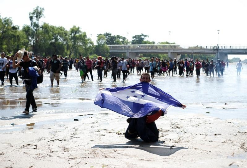 A migrant, part of a caravan travelling to the U.S., holds a Honduran flag as he cross the Suchiate river at the border between Guatemala and Mexico, in Ciudad Hidalgo, Mexico, January 20, 2020. 