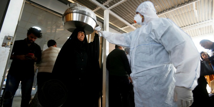 An Iraqi medical staff member checks a passenger’s temperature, amid the new coronavirus outbreak,