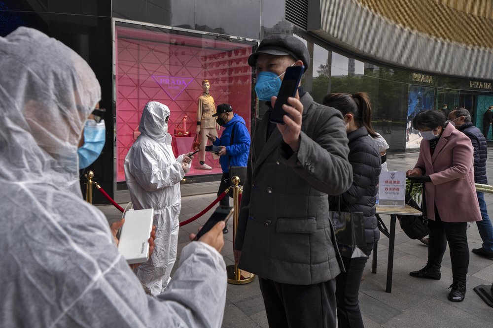 In this photo released by Xinhua News Agency, workers wearing protective suits check customers' health QR codes at the entrance of a re-opened shopping mall in in Wuhan in central China's Hubei province, Monday, March 30, 