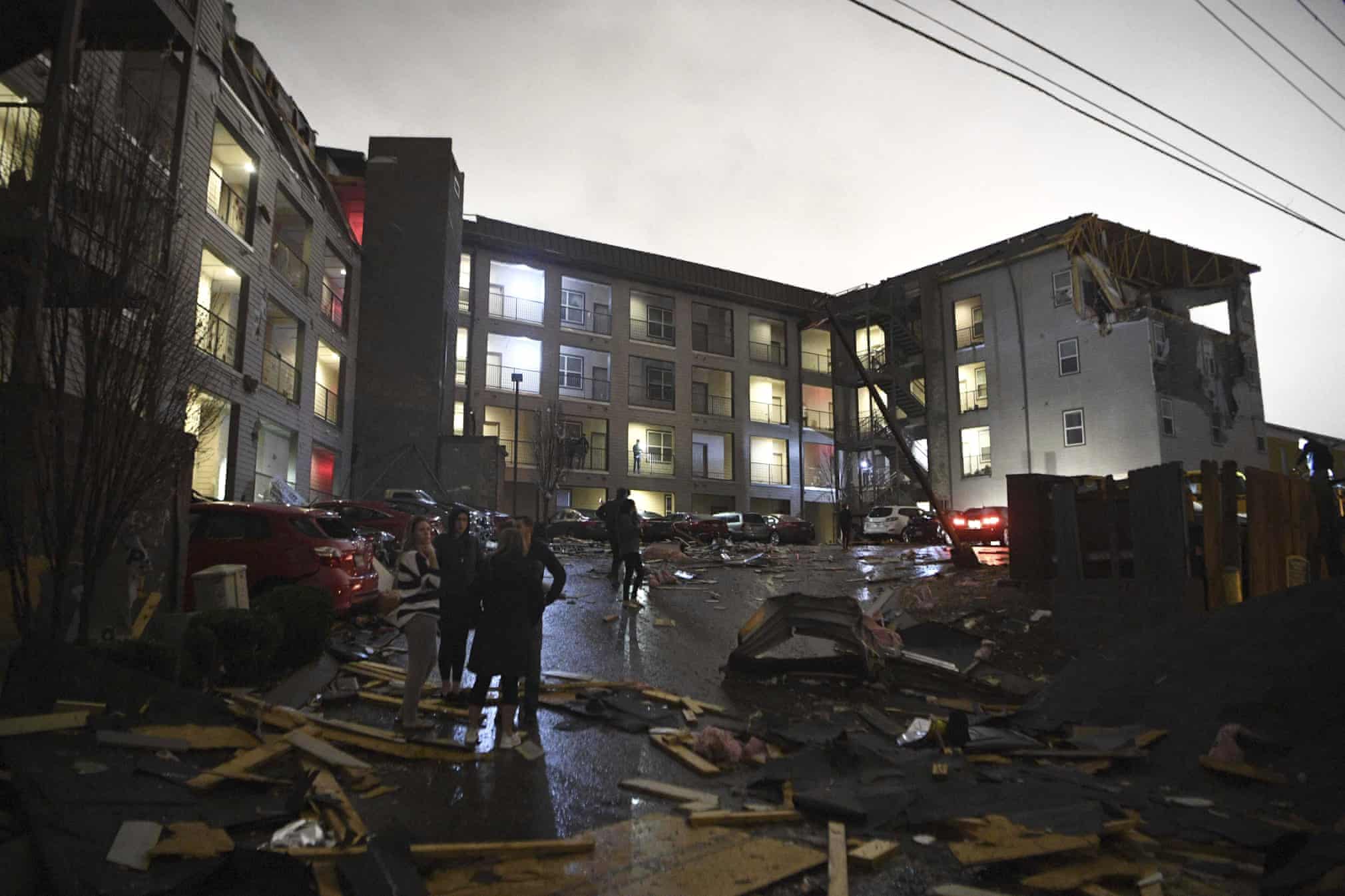 As the sky lightens, debris is scattered across the parking lot of a damaged apartment building Photograph: Courtney Pedroza/AP