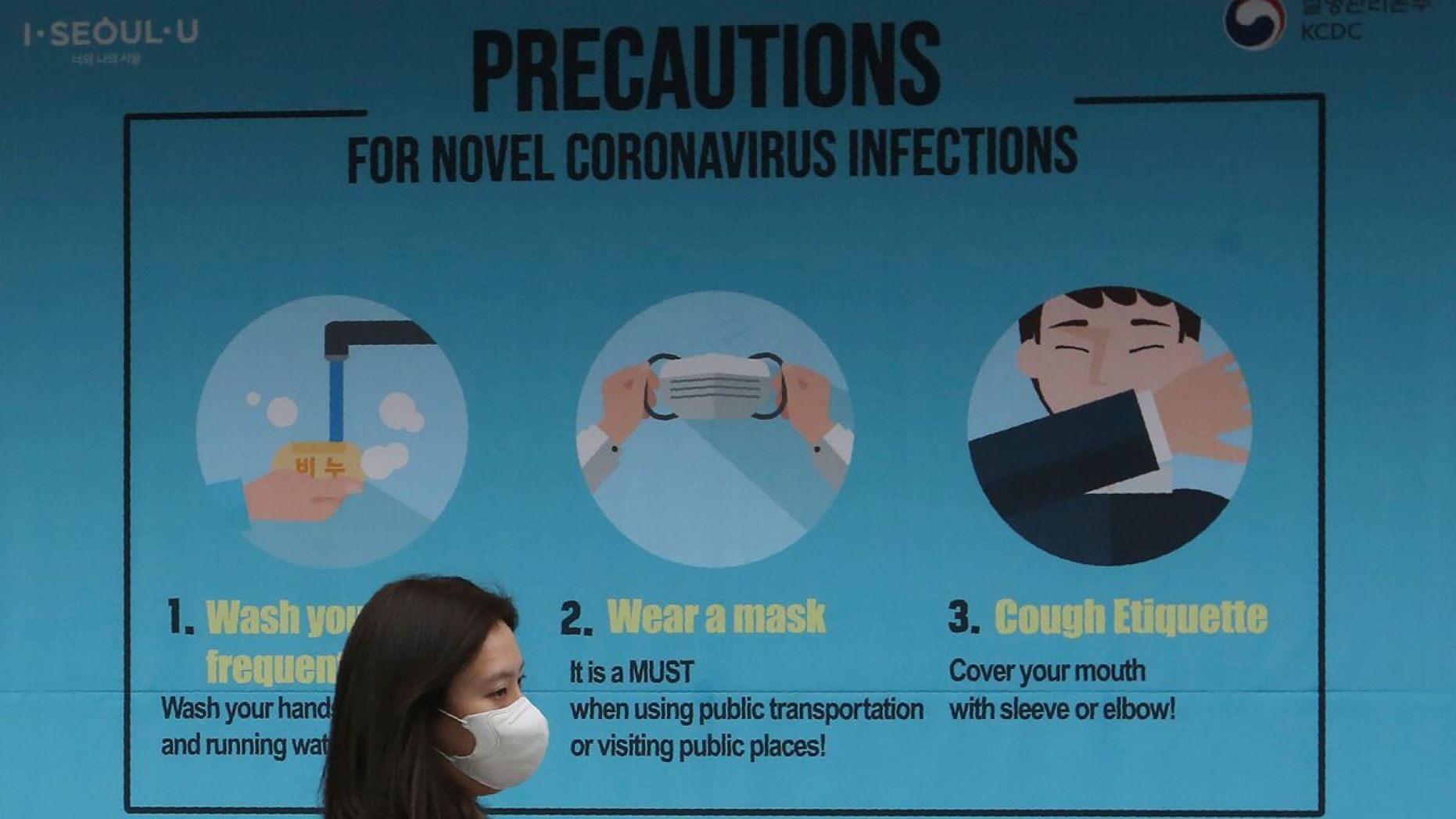 A woman wearing a face mask passes by a poster about precautions against the coronavirus in Seoul, South Korea,
