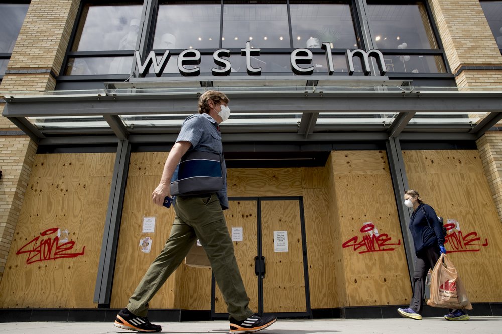 People in masks walk past a boarded up storefront along 14th Street in Northwest Washington, Wednesday, April 29, 2020. 