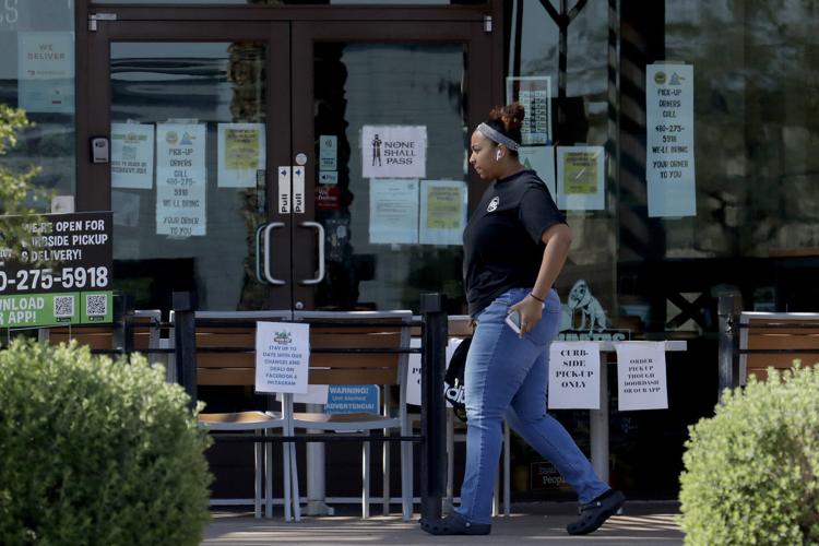 A person passes a temporary take-out only restaurant Friday, March 27, 2020, in Phoenix. Arizona