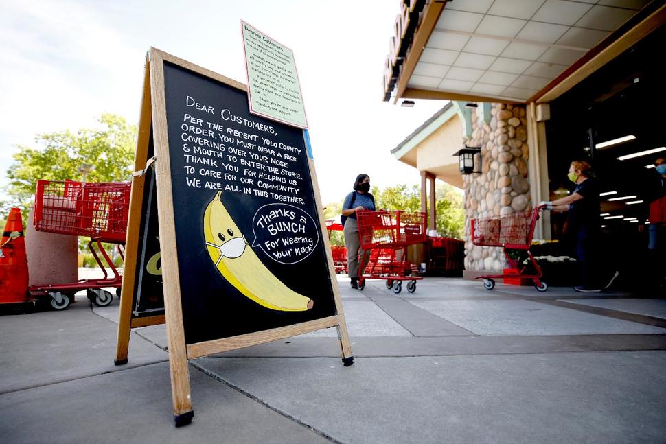 A drawing of a banana wearing a face mask advises customers they must wear a covering over their mouth and nose before entering a Trader Joe's in Davis, Calif., Monday, April 27,