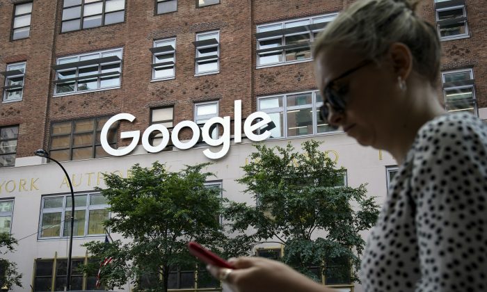 A woman looks at her smartphone as she walks past Google Building 8510 at 85 10th Ave., New York City, N.Y., on June 3, 2019.