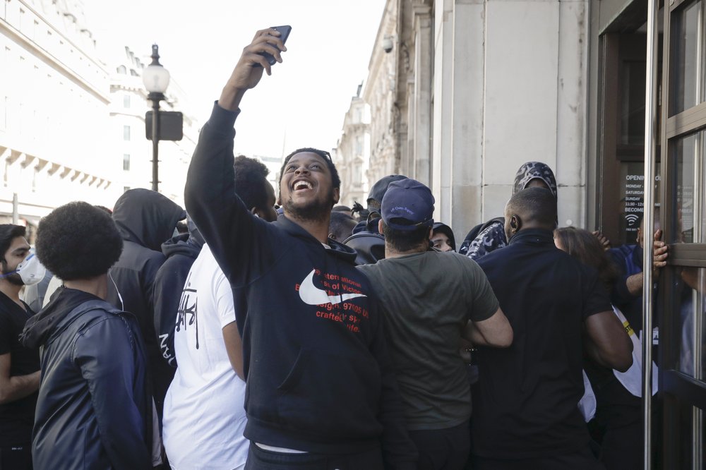 A youth takes pictures as people queueing push to enter the Niketown shop in London, Monday, June 15, 2020. After three months of being closed under coronavirus restrictions,