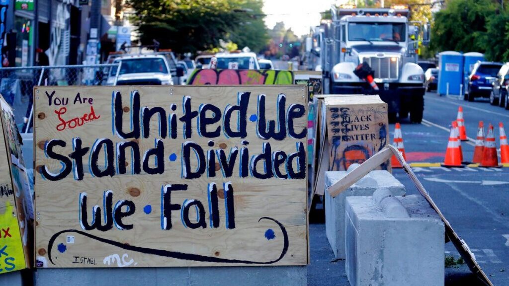 A sign on a barricade reads "United we stand divided we fall," as a truck and other heavy equipment from the Seattle Department of Transportation is staged at the CHOP ,