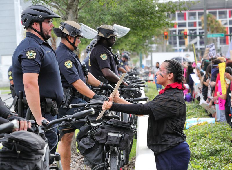 A protestor holds up a sign in front of Orlando Police officers lined up in front of OPD headquarters on June 2, 2020.