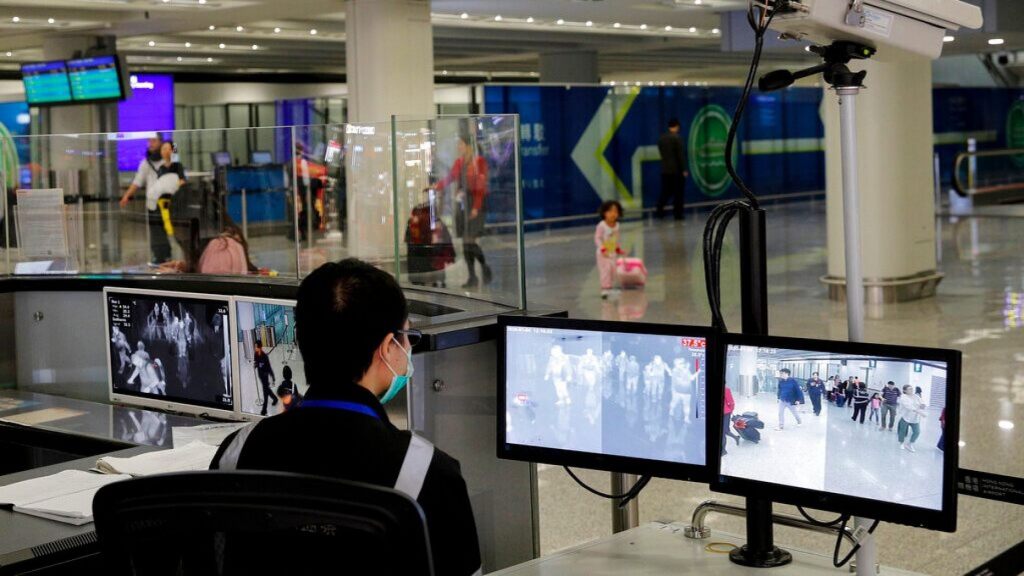 In this Jan. 4, 2020, file photo, a health surveillance officer monitors passengers arriving at the Hong Kong International airport in Hong Kong.