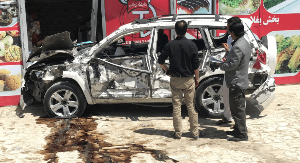 Afghans look at at a car hit damaged a suicide bomb blast in Kabul, Afghanistan.