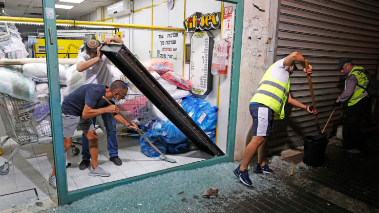 Israeli men remove the shattered glass window of a laundry shop following a rocket attack fired from the Gaza Strip and crashed in the southern coastal city of Ashdod on September 15, 2020.