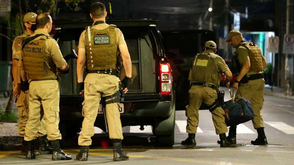 Military police officers carry a bag filled with money left behind by armed bank robbers, in Criciuma, Santa Catarina state, Brazil, Tuesday, Dec. 1, 2020. Dozens of criminals armed with assault rifles invaded the city in southern Brazil overnight and took control of the streets as they assaulted a local bank. (Guilherme Hahn/Futura Press via AP)