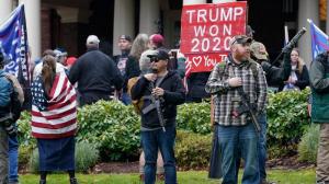Supporters of President Trump, including those with guns and a bat, stand outside the Governor's Mansion after breaching a perimeter fence, Wednesday, Jan. 6, 2021, at the Capitol in Olympia, Wash.