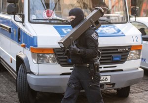 A police walks in front of a car during raids against an Islamist network at the Maerkische Viertel neighborhood in Berlin, Thursday, Feb. 25, 2021. Police searched the apartments of several alleged supporters of a banned Islamic extremist organization in the German capital.