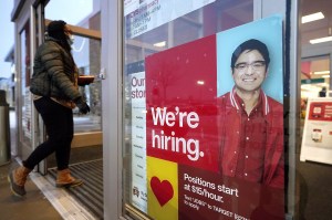 A passerby walks past an employment hiring sign while entering a Target store location in Westwood, Mass.