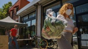 Fashion designer Josie Vand wears a facemask as she retrieves a bag with organic vegetables from a farm box from County Line Harvest in Los Angeles on Friday, April 2, 2021.