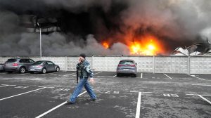 A Ukrainian serviceman walks past as fire and smoke rises over a damaged logistic center after shelling in Kyiv, Ukraine, Thursday, March 3, 2022. (AP Photo/Efrem Lukatsky)