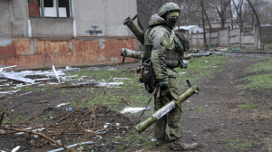 An armed serviceman of Donetsk People's Republic militia walks past a building damaged during fighting in Mariupol on Wednesday. (AP/Alexei Alexandrov)
