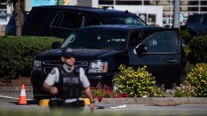 A police officer standing near a windshield and passenger window of an RCMP vehicle with bullet holes at the scene of a shooting in Langley, British Columbia, Monday, July 25, 2022.  ((Darryl Dyck/The Canadian Press via AP))