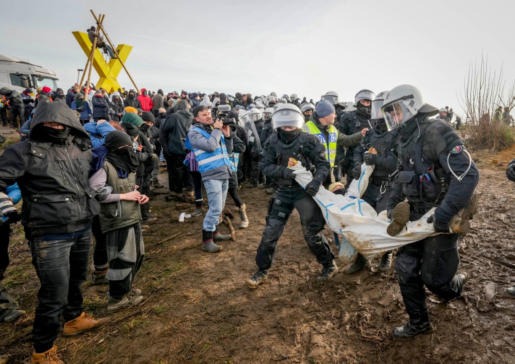 Police officers carry a demonstrator to clear a road at the village Luetzerath near Erkelenz, Germany, Tuesday, Jan. 10, 2023. The village of Luetzerath is occupied by climate activists fighting against the demolishing of the village to expand the Garzweiler lignite coal mine near the Dutch border. (AP Photo/Michael Probst)